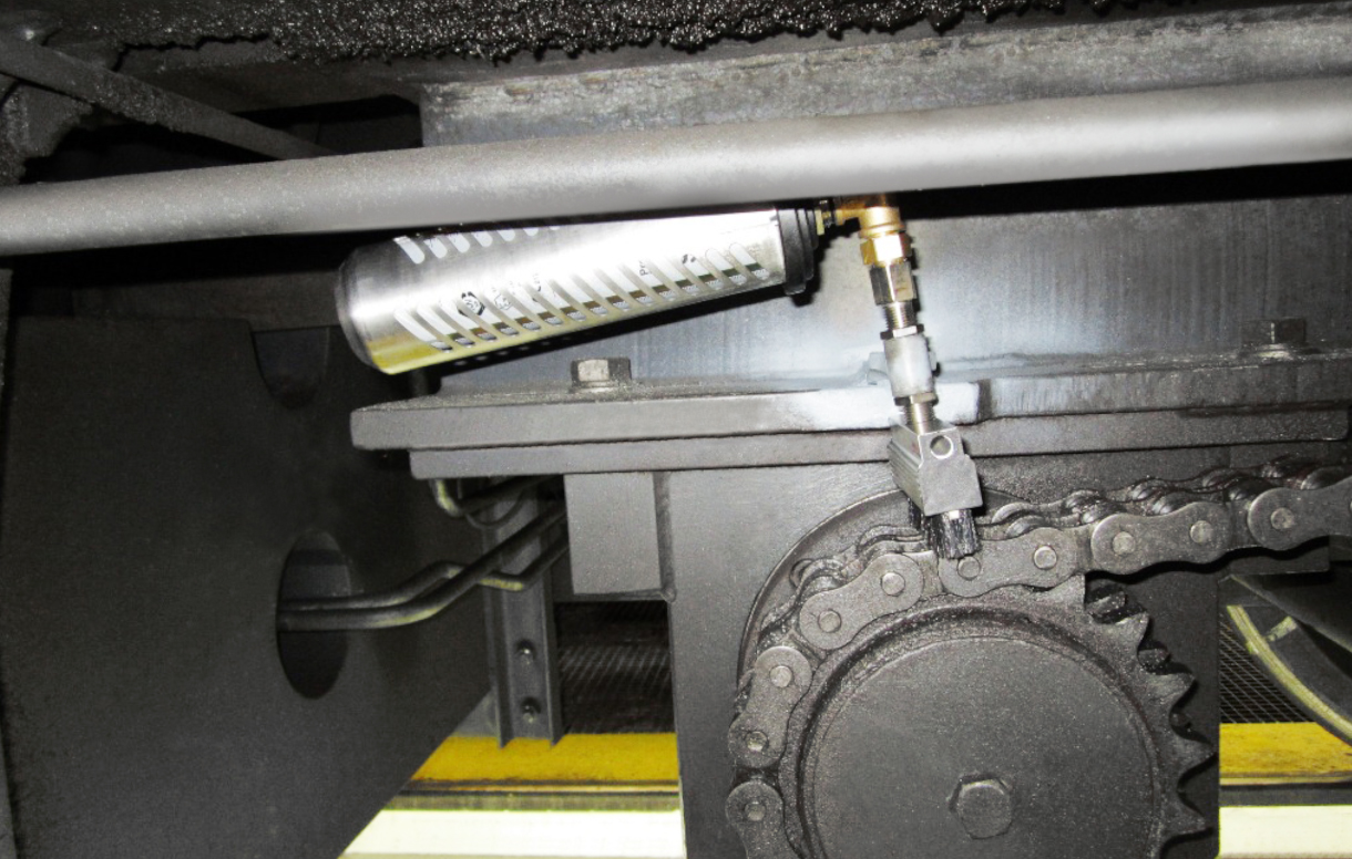 El lubricador simalube de 250 ml lubrica la cadena de transmisión de una grúa de construcción sobre raíles. Además, el dispensador está protegido por una tapa protectora.