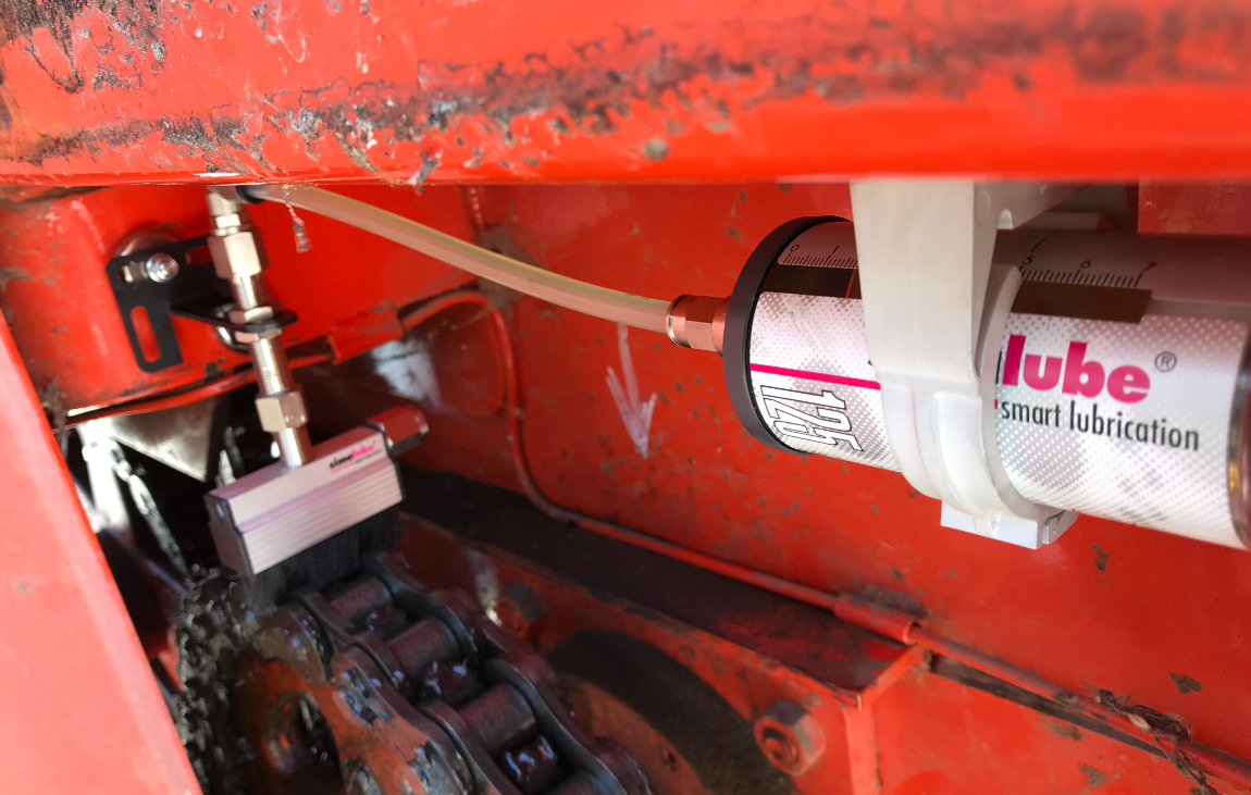 La cadena de un vehículo de recolección agrícola se lubrica automáticamente con un lubricador simalube y también se limpia al mismo tiempo gracias al cepillo aplicado.